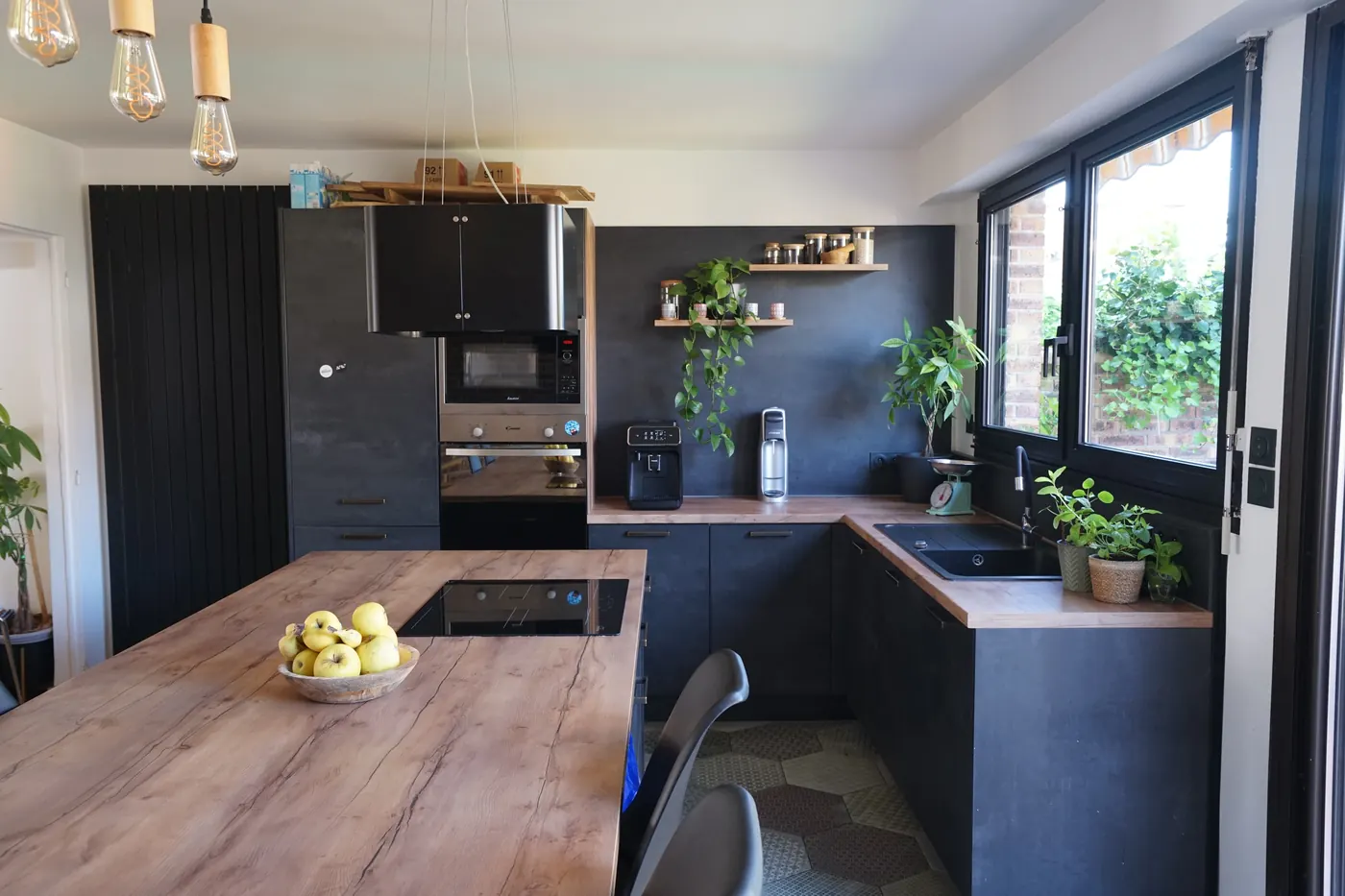 La cuisine rénovée : meubles noirs, îlot en bois, baie sur le jardin