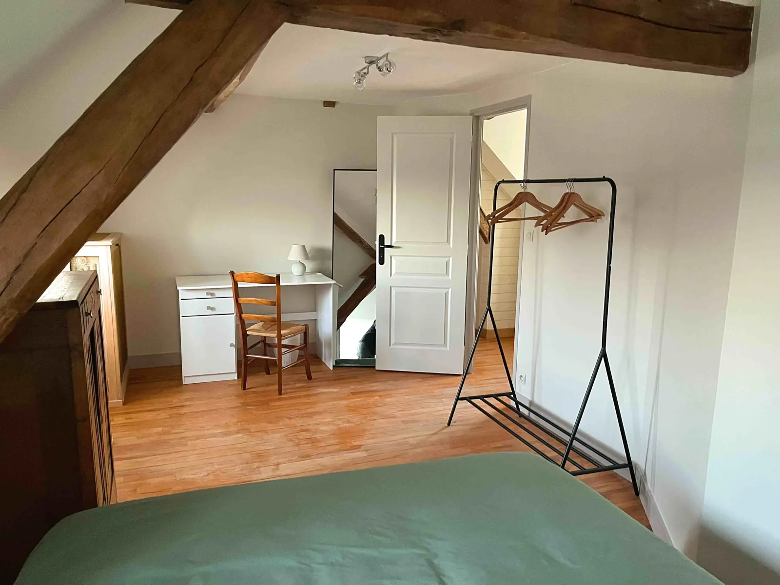 La chambre sous les combles après les travaux : murs blancs, parquet, poutres conservées